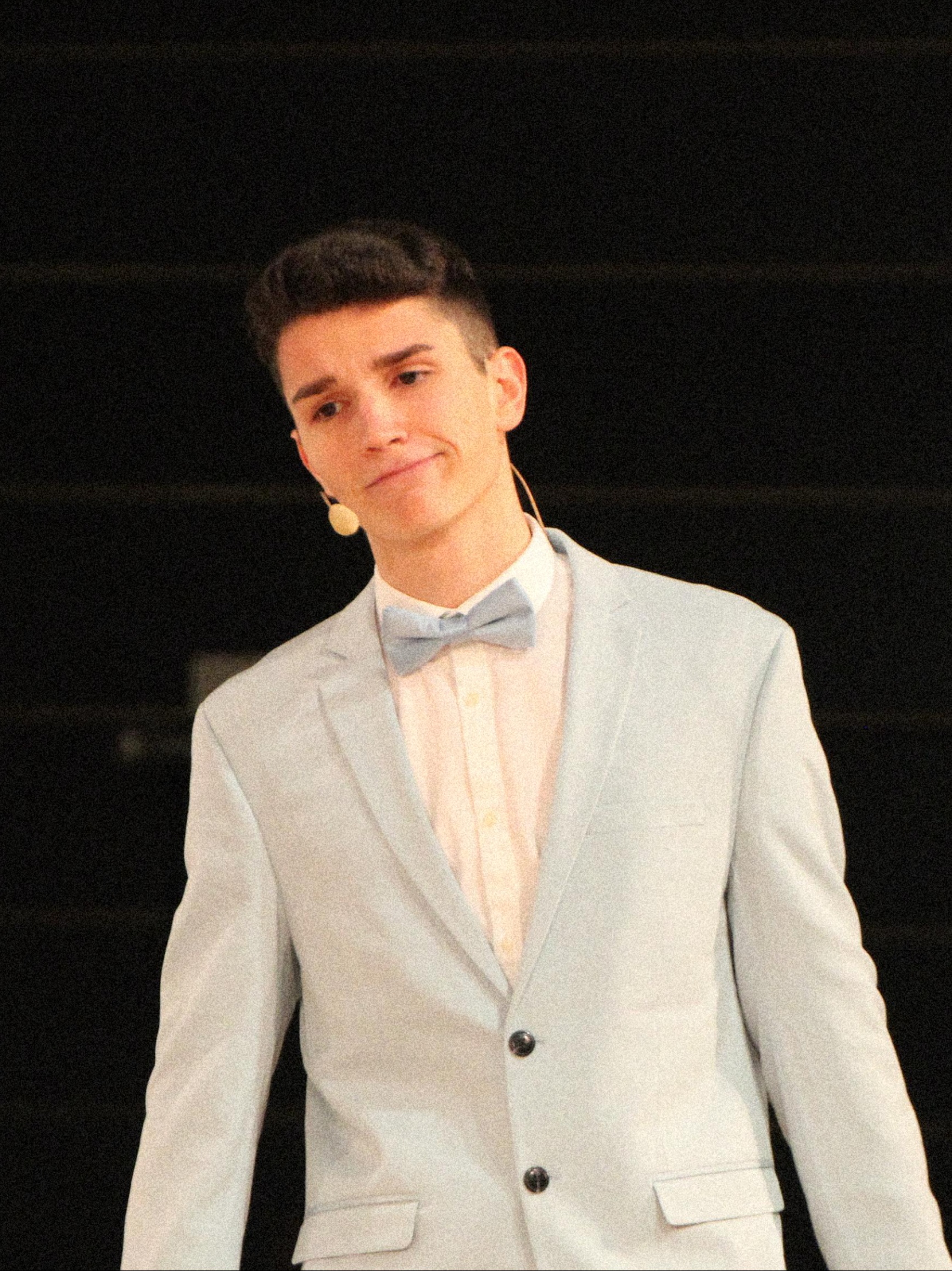 Linus Kern presenting on stage in light blue suit with bow tie - public speaker and consultant